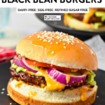 a homemade sweet potato black bean burger filled with red onion, mashed avocado, lettuce, tomato, vegan burger sauce in a sesame burger bun