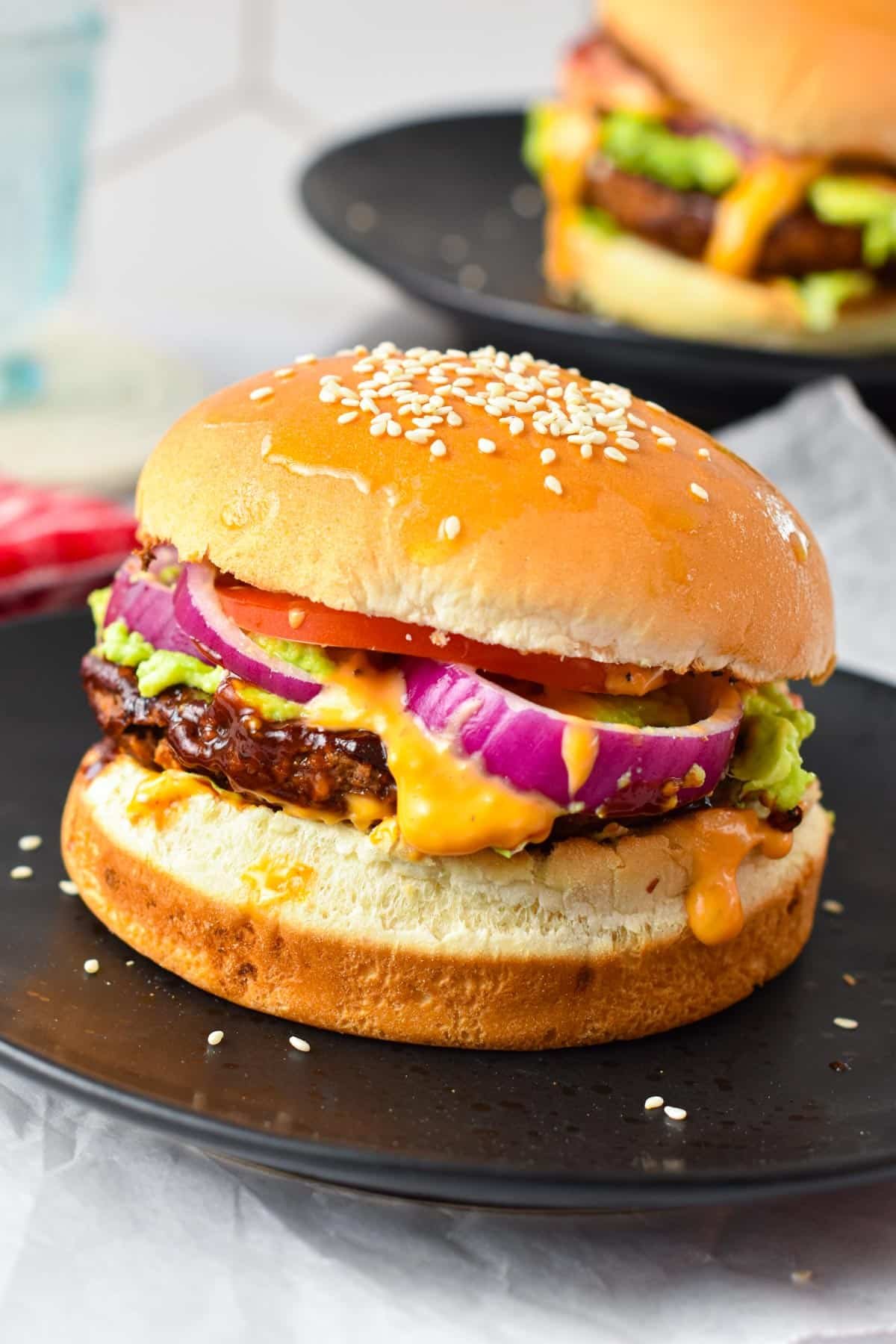 A homemade sweet potato black bean burger filled with red onion, mashed avocado, lettuce, tomato, vegan burger sauce in a sesame burger bun