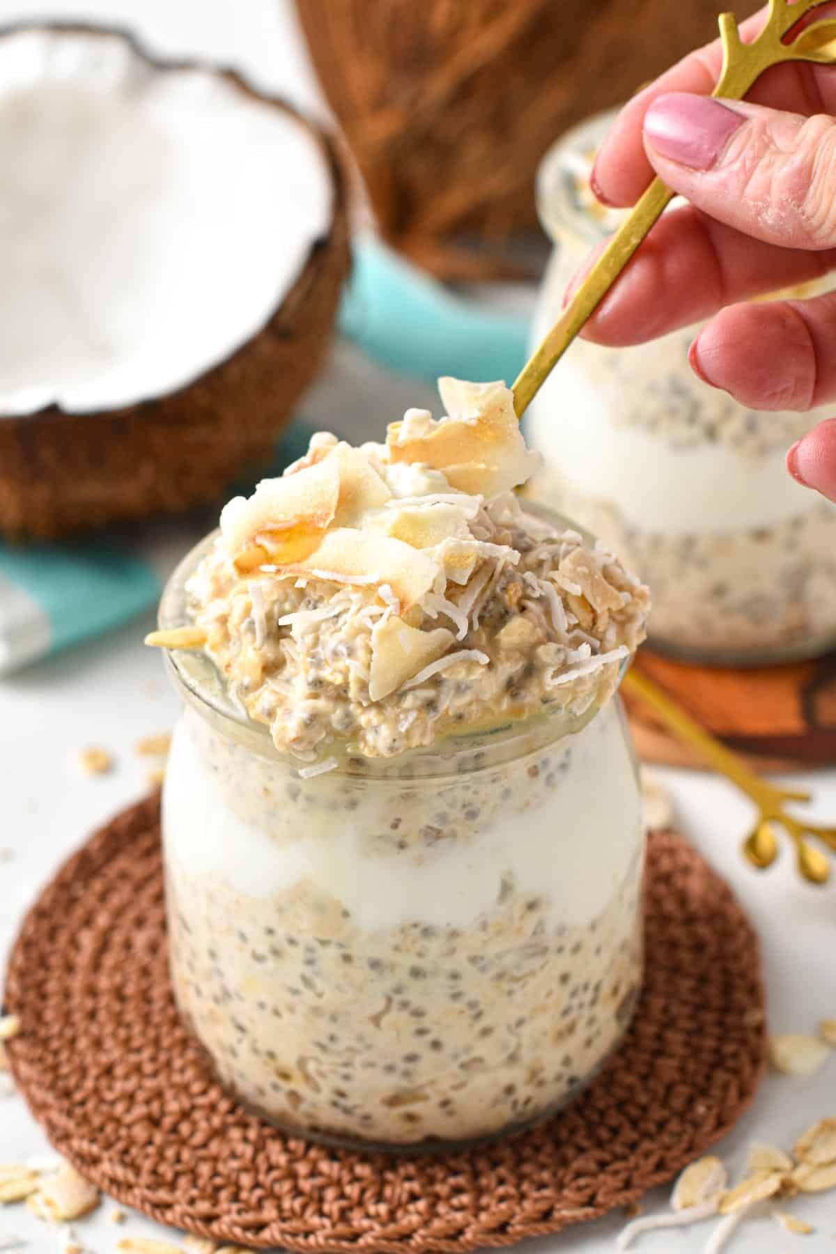 Coconut Overnight Oats in a mason jar with a golden spoon taking some out.