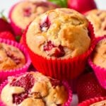 a stack of vegan strawberry muffins with a lovely golden fluffy crumb filled with juicy pieces of baked strawberries