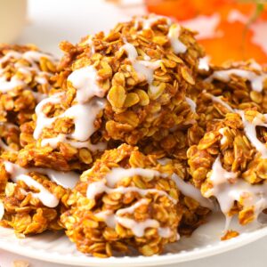 a plate filled with a stack of no-bake pumpkin cookies topped with a drizzle of icing sugar