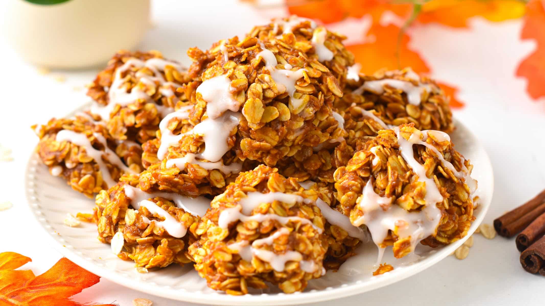 A plate filled with a stack of no-bake pumpkin cookies topped with a drizzle of icing sugar.
