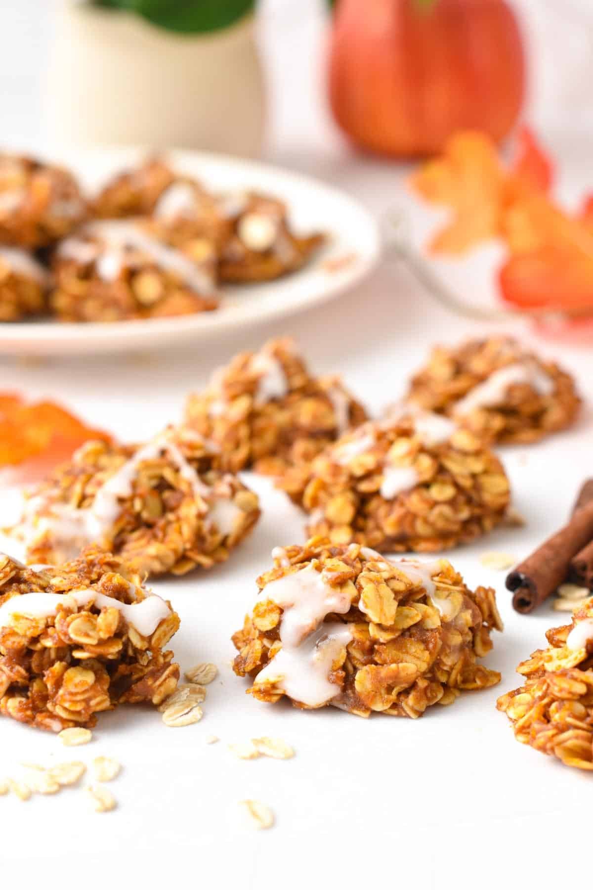 A plate filled with a stack of no-bake pumpkin cookies topped with a drizzle of icing sugar.