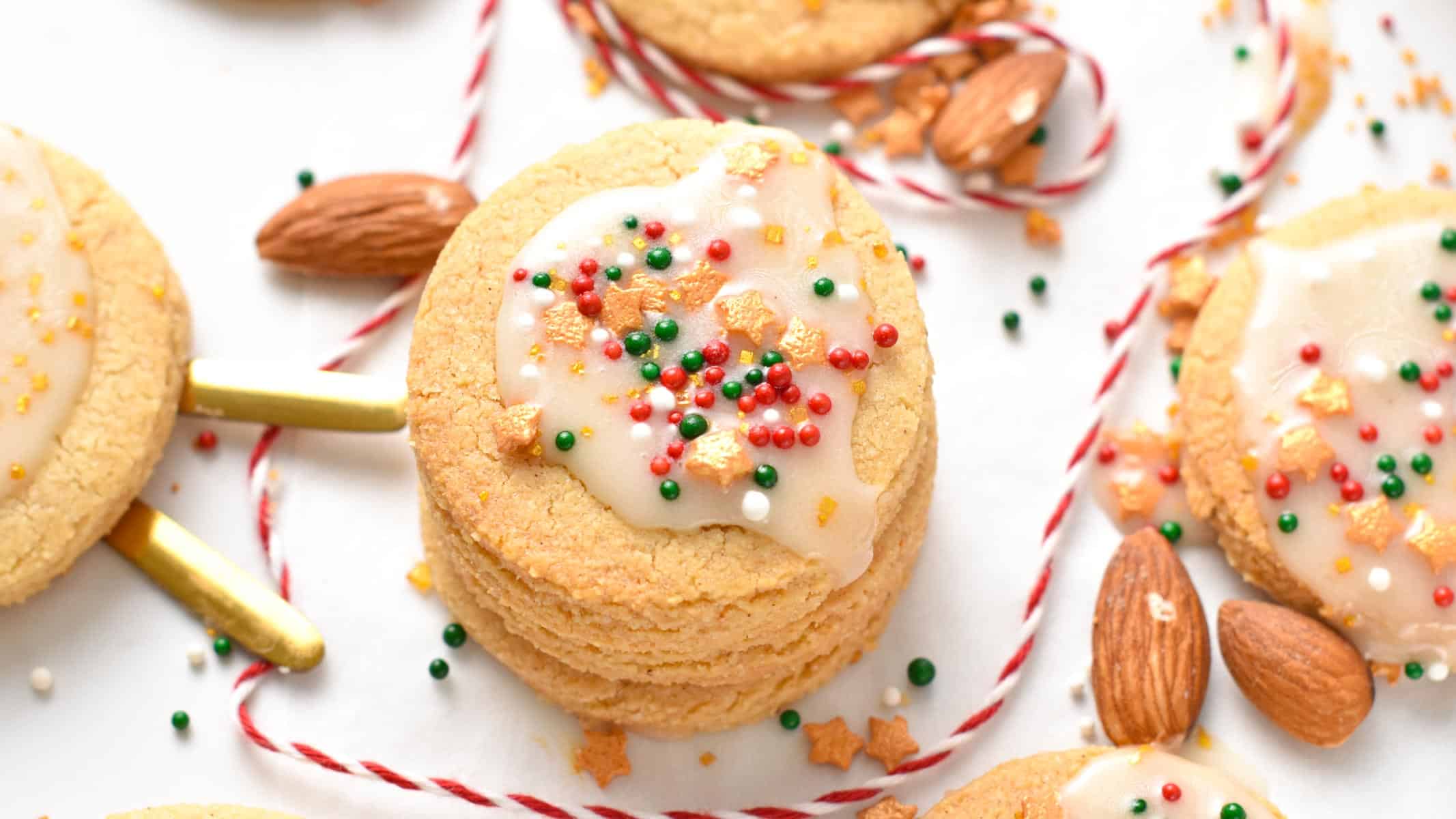 A stack of almond flour sugar cookies with royal icing and red, green, and golden sprinkles on top.