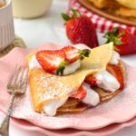 a vegan french crepe filled with strawberries, dairy-free whipped cream and lots of vegan crepes in the background