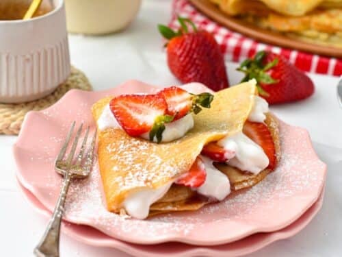 a vegan french crepe filled with strawberries, dairy-free whipped cream and lots of vegan crepes in the background