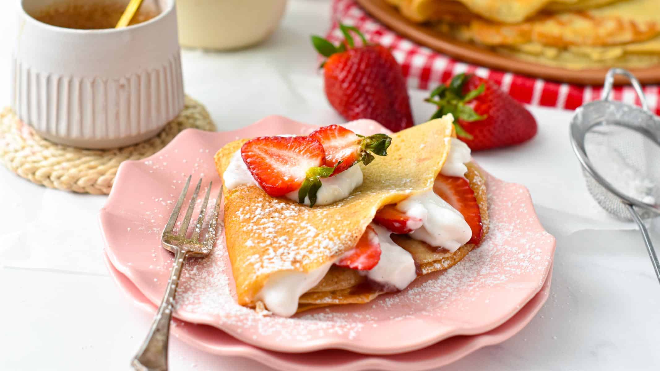 a vegan french crepe filled with strawberries, dairy-free whipped cream and lots of vegan crepes in the background