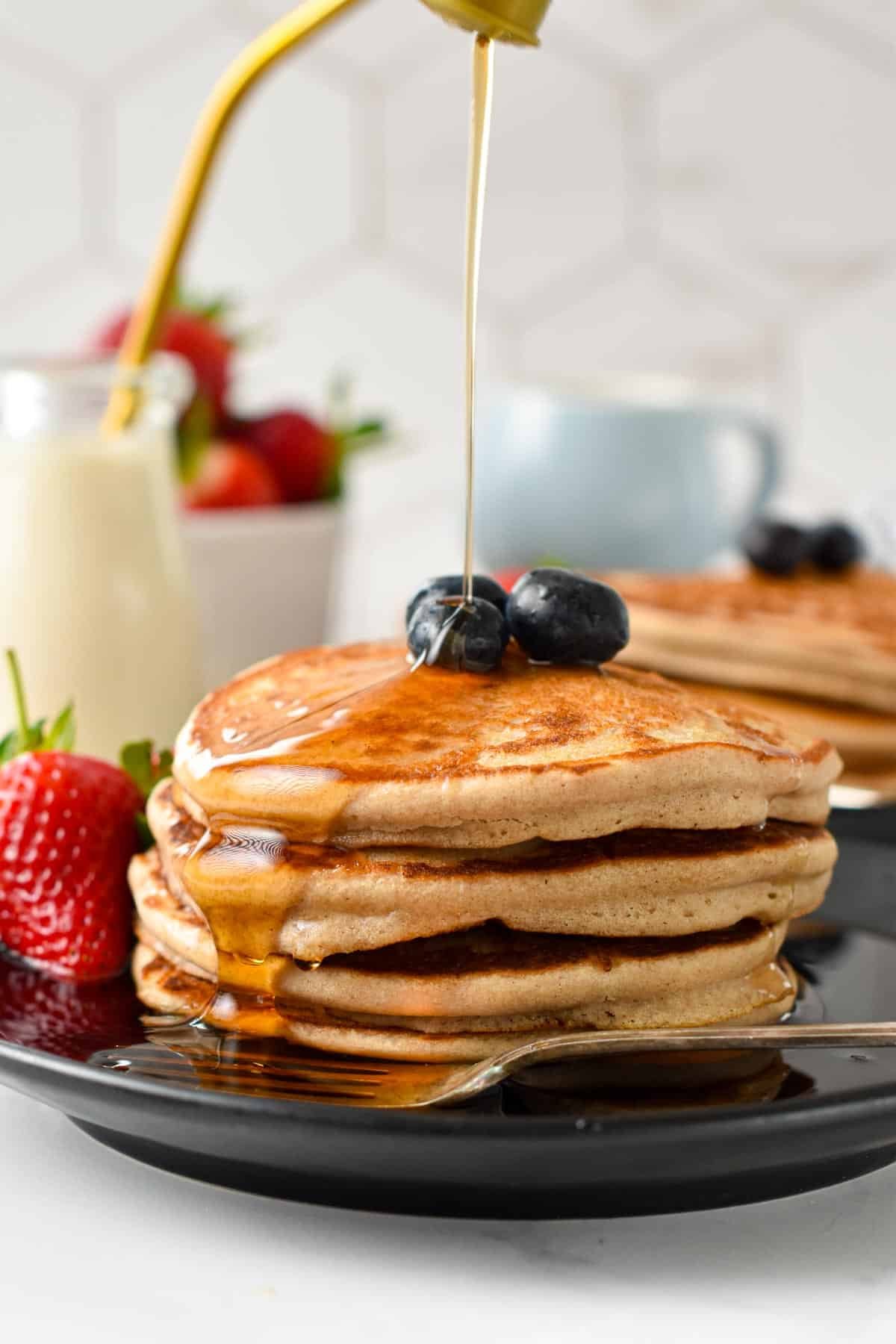 A stack of three vegan buckwheat pancakes with blueberries on top and a drizzle of maple syrup.