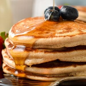 a stack of three vegan buckwheat pancakes with blueberries on top and a drizzle of maple syrup