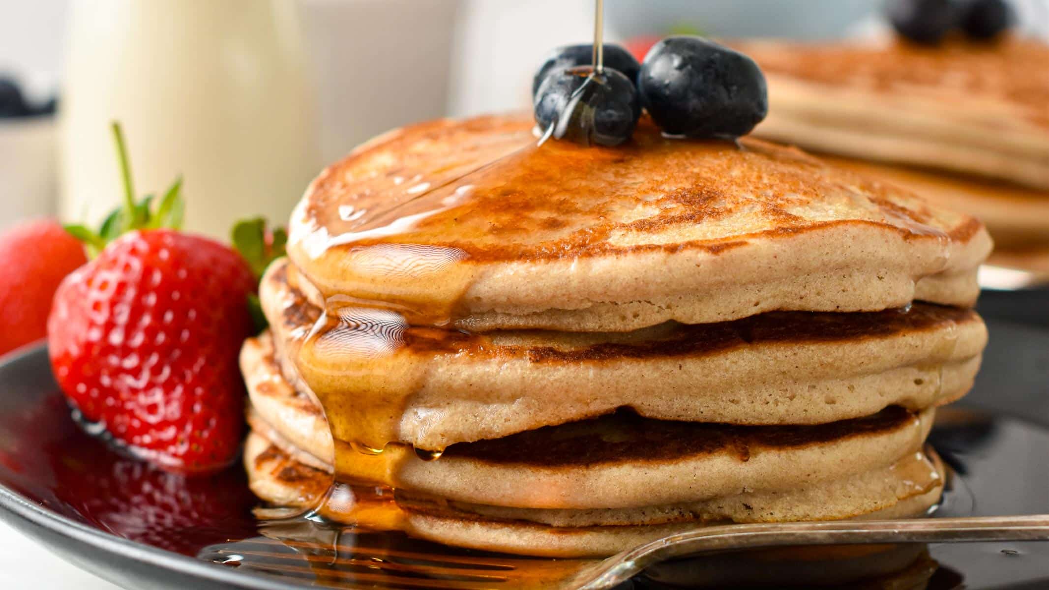 a stack of three vegan buckwheat pancakes with blueberries on top and a drizzle of maple syrup