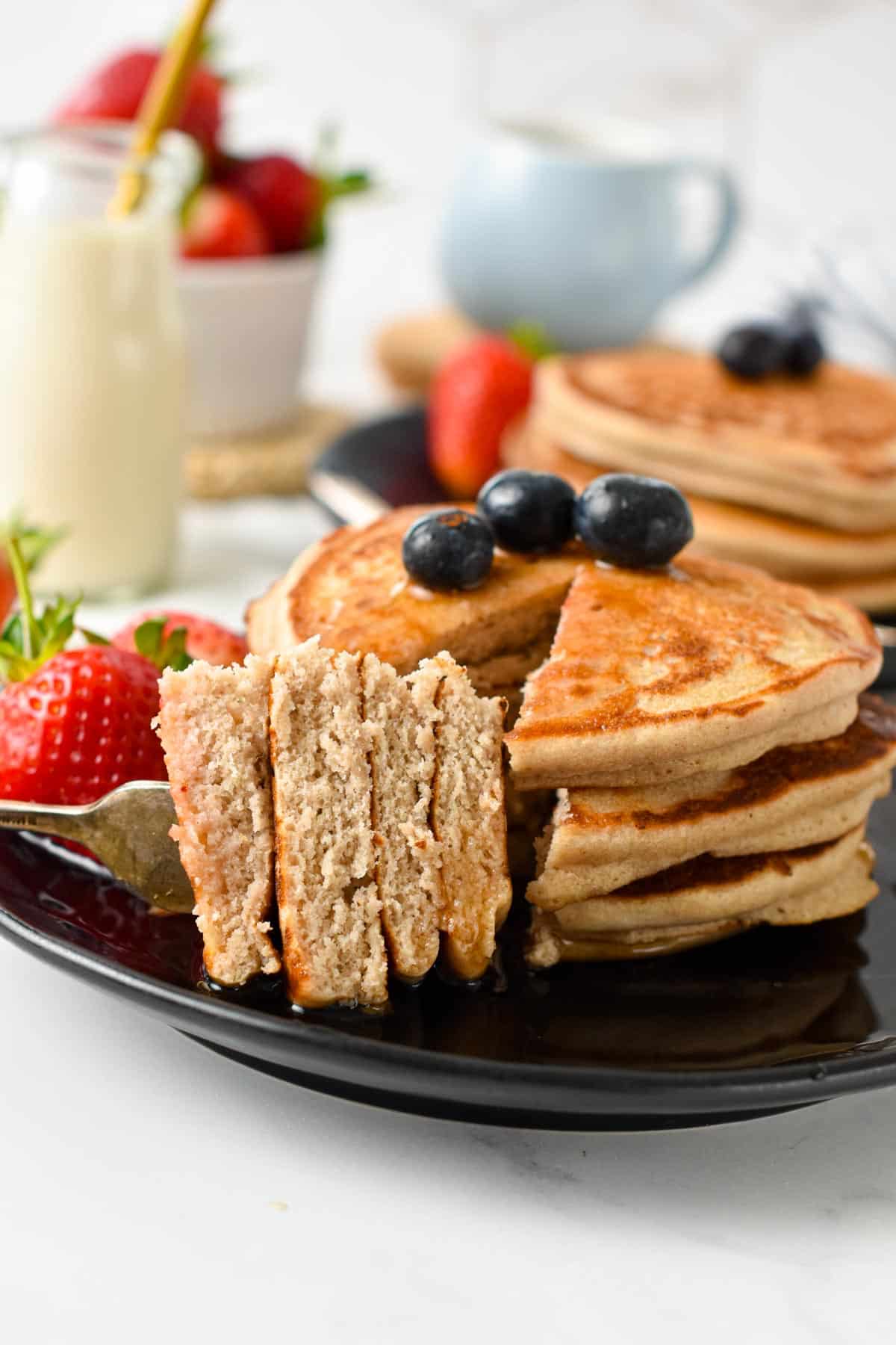 A stack of vegan buckwheat pancakes sliced with a fork holding some pancakes and showing the fluffy pancake texture.