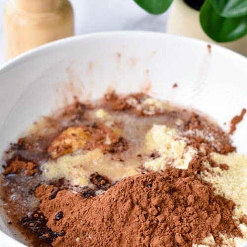 A bowl filled with almond flour, melted coconut oil, maple syrup, and unsweetened cocoa powder.