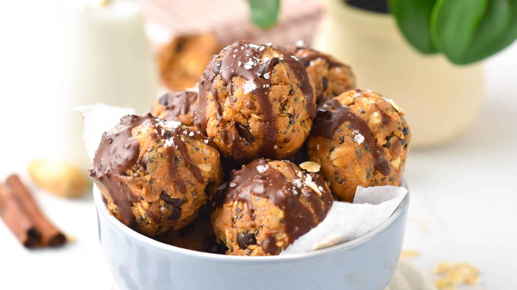 No-bake peanut butter protein balls in a large blue bowl and decorated with a drizzle of melted chocolate and shredded coconut.