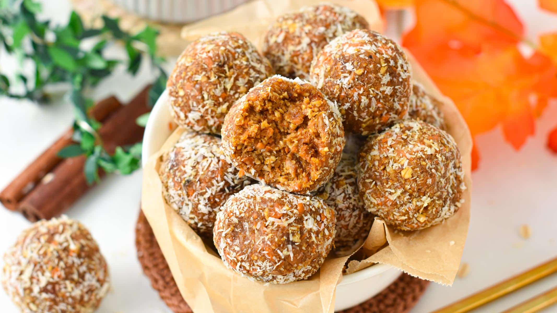 No-bake carrot cake energy bites in a bowl with parchment paper next to an autumn decor.