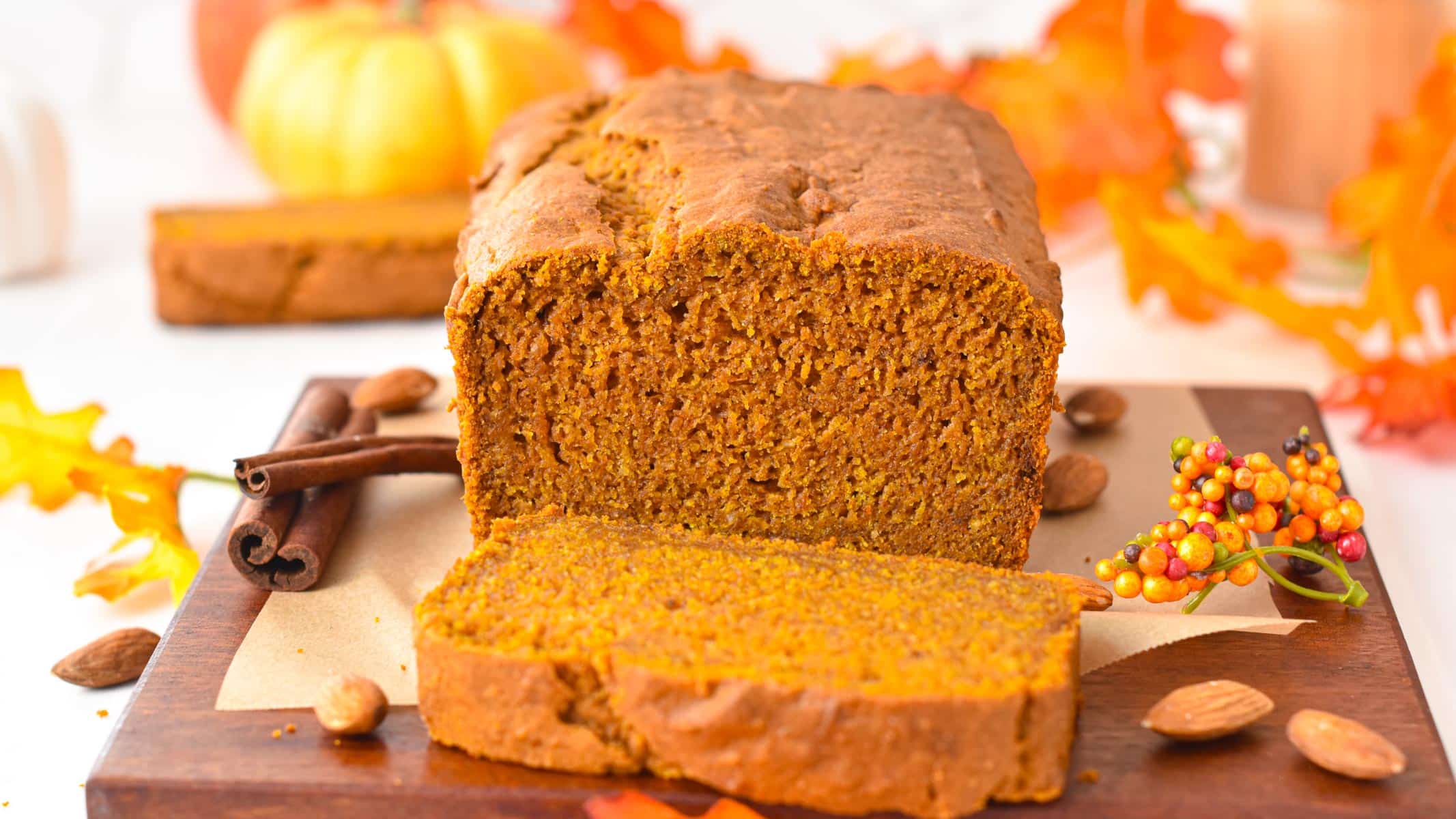 A sliced vegan gluten-free pumpkin bread with fall decoration in the background.