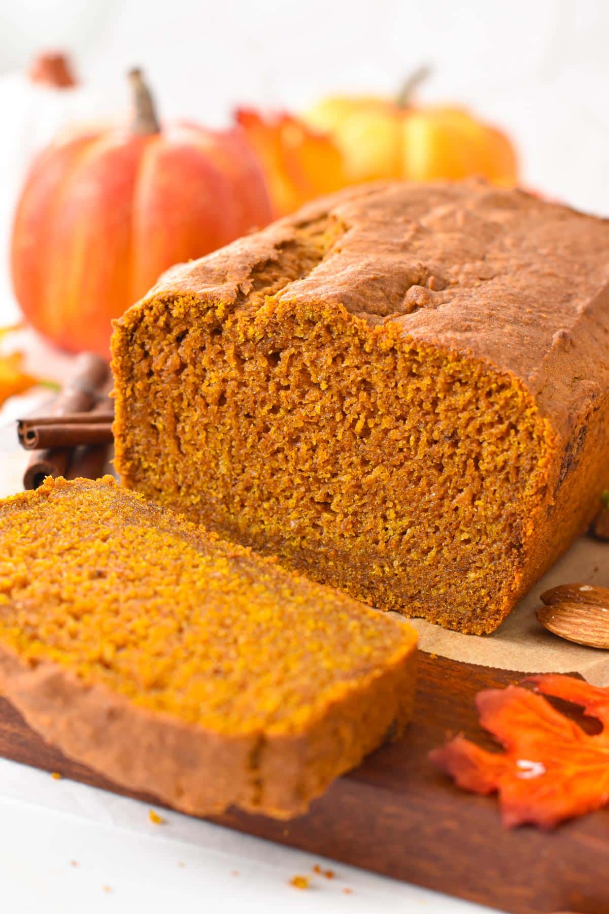 Vegan gluten-free pumpkin bread loaf on a wooden board with fall decoration in the background.