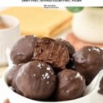 a bowl filled with no-bake brownie protein balls with one ball showing the inside chocolate fudge texture