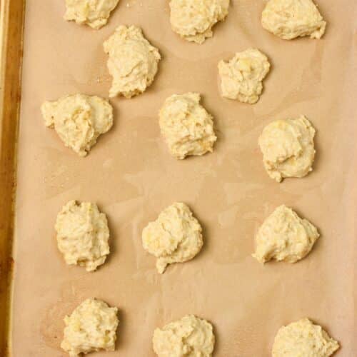 dollops of banana cookie dough on a baking sheet lined with brown parchment paper