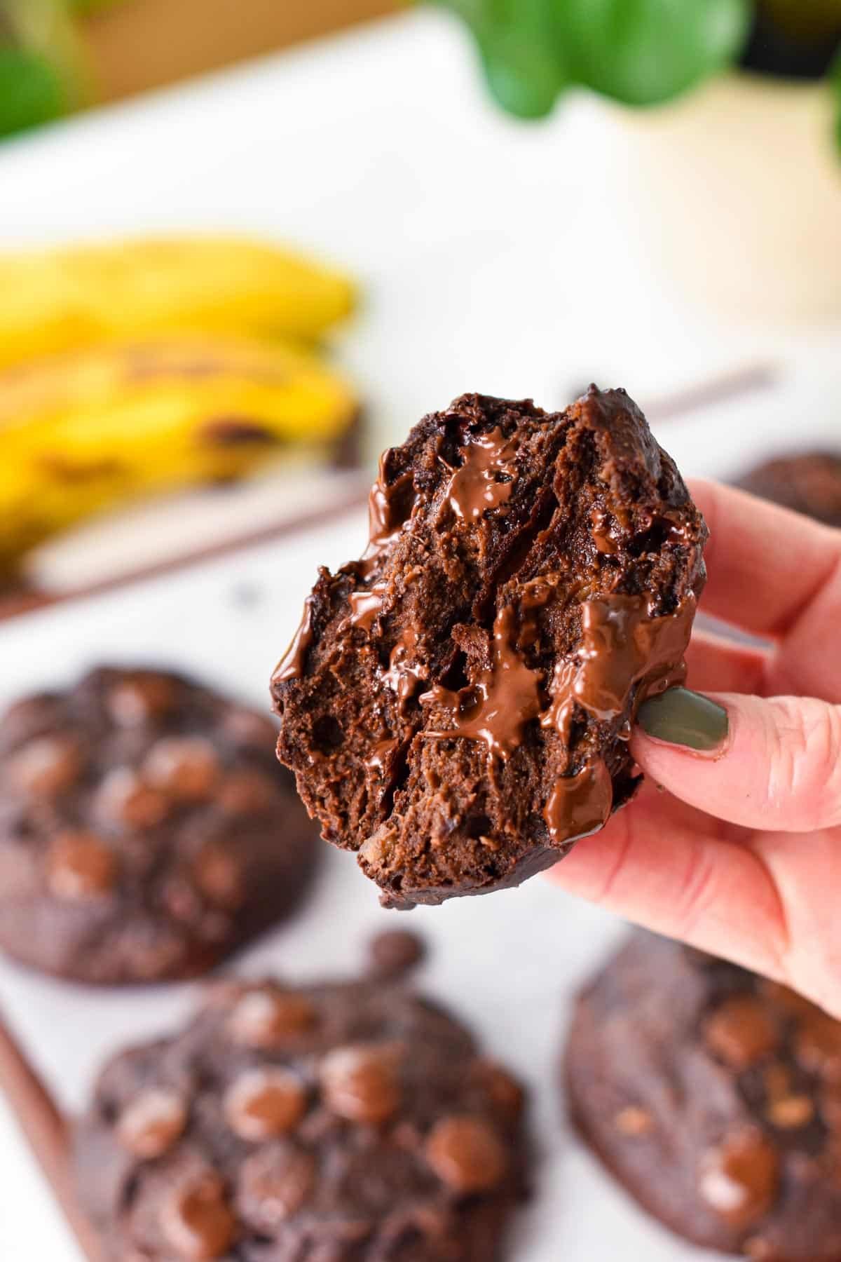 a hand holding two halves of a chocolate banana cookies showing the extra fudgy chocolate texture