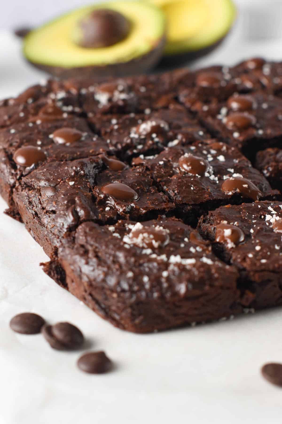 Avocado Brownies sliced on a table in front of an open avocado.