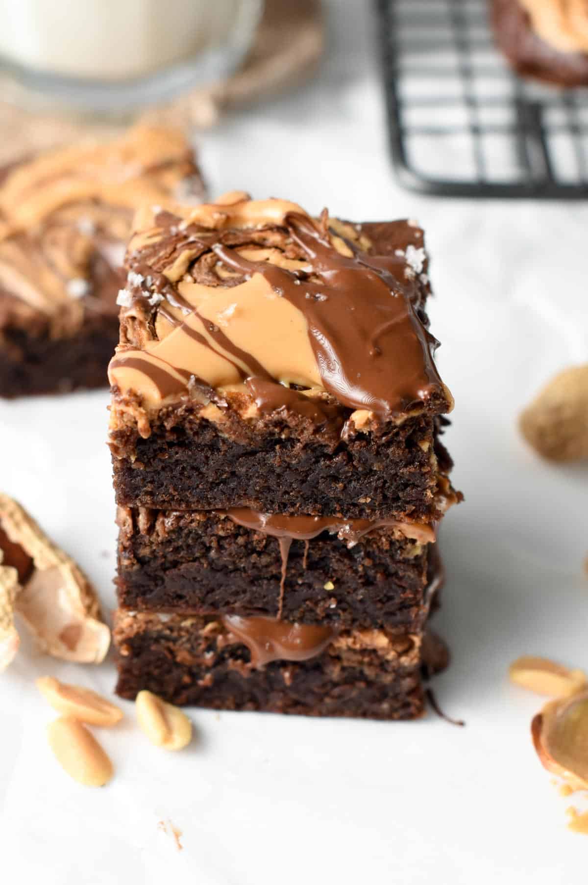 Vegan banana peanut butter brownies stacked on a white table and decorated with melted chocolate and peanut butter.