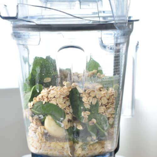 a blender jug filled with the ingredients for banana spinach pancakes: oats, bananas plant-based milk, vanilla