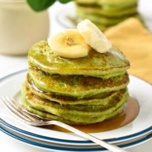 a stack of green spinach banana pancakes with banana slices on top and a drizzle of maple syrup
