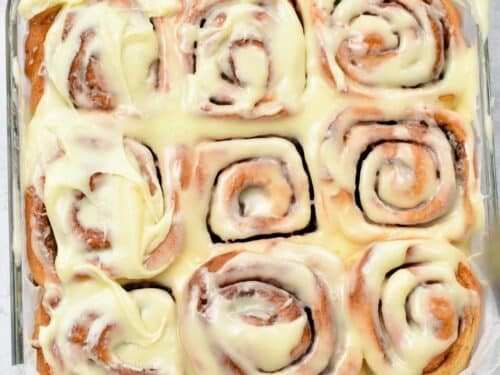 a picture of 9 vegan cinnamon rolls baked in a glass pan, and iced with vegan cream cheese