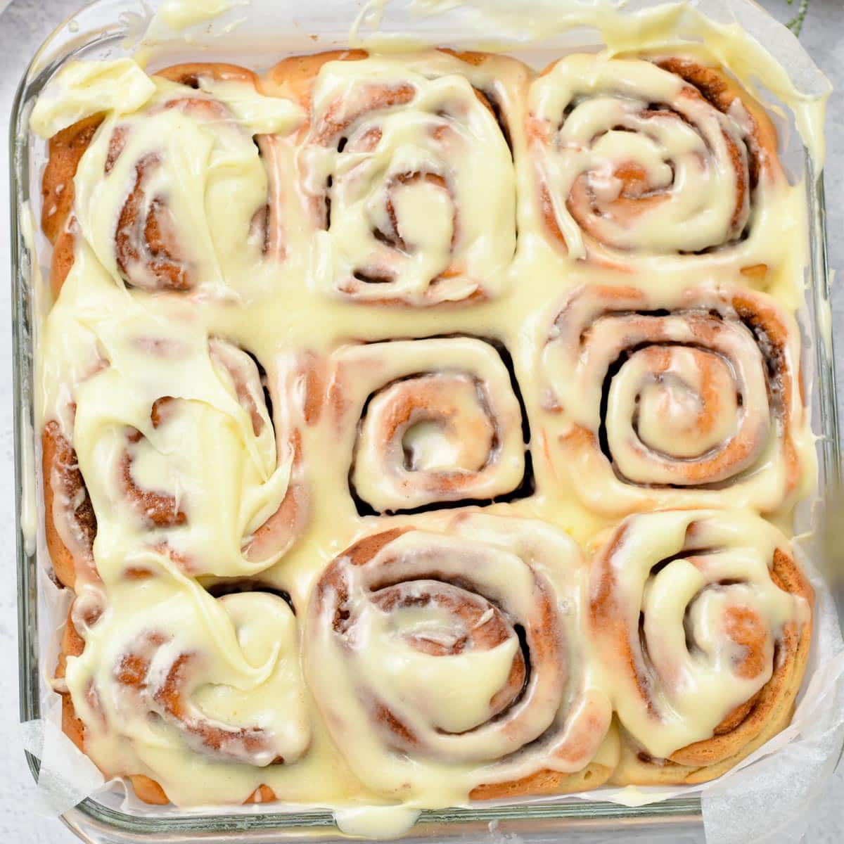 a picture of 9 vegan cinnamon rolls baked in a glass pan, and iced with vegan cream cheese