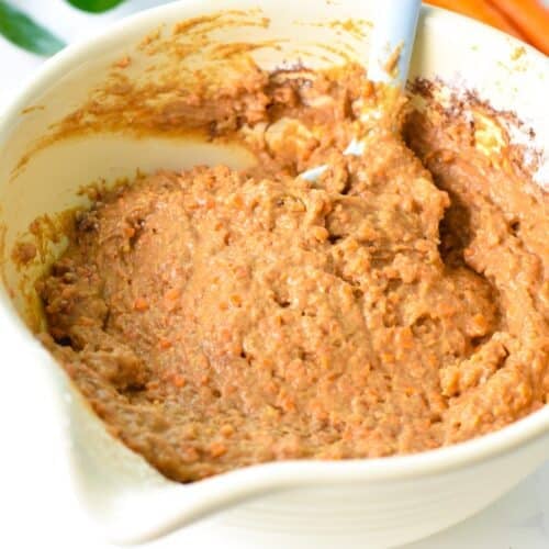 a mixing bowl with carrot cake batter and a light blue silicone spatula in the bowl