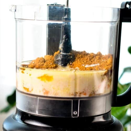 A food processor bowl with carrots, oil, nondairy milk, applesauce, coconut sugar, and vanilla extract. 