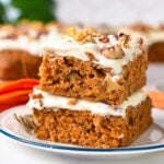 two slices of sheet pan carrot cake, frosted, and stacked on a plate with in the background a carrot cake and green plant