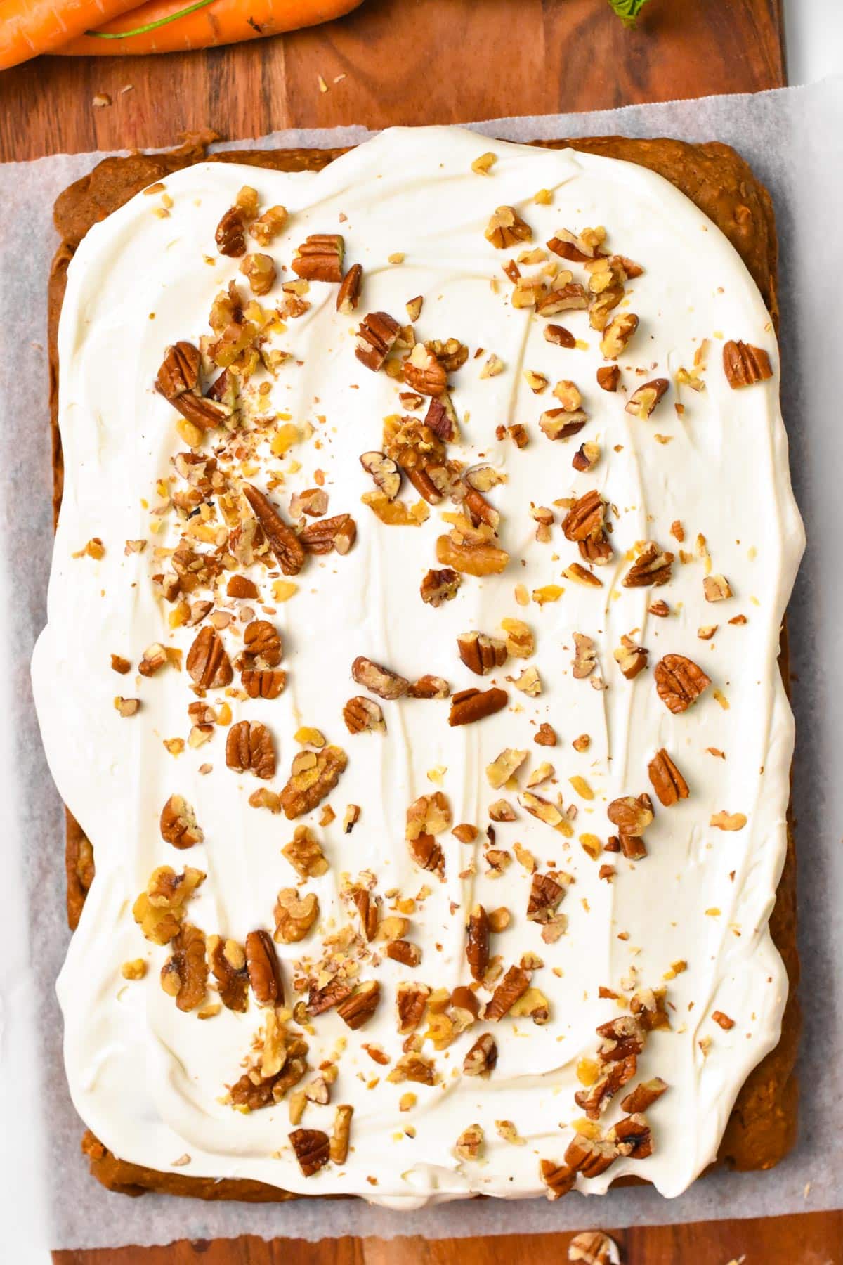 a picture from the top of a sheet pan vegan carrot cake with frosting and chopped walnuts