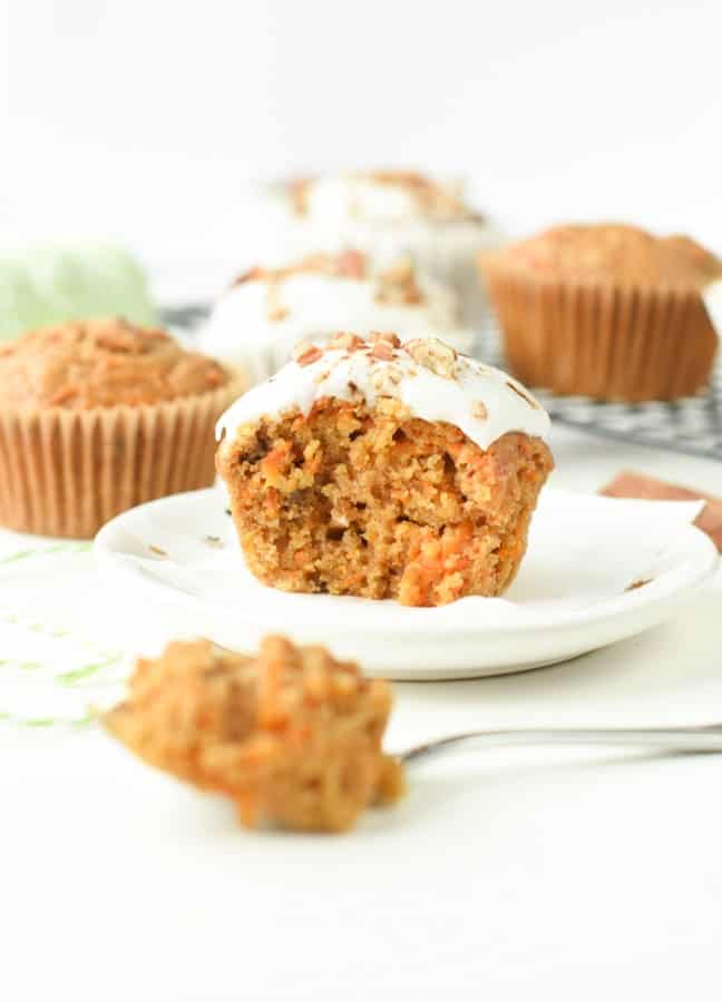 Vegan carrot cake cupcakes with vegan frosting on a small plate with a bite taken on a fork.