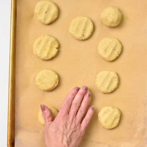A hand flattening the almond flour banana cookie dough balls on a baking sheet.