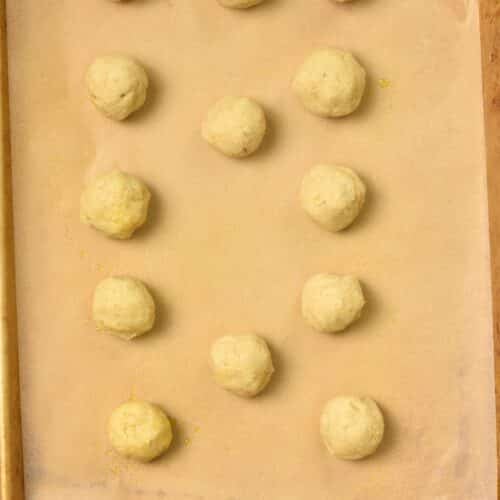 A baking sheet lined with brown parchment paper and almond flour banana cookie dough balls on the sheet.