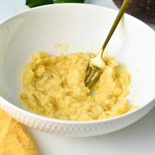 A golden fork in a mixing bowl with mashed bananas.