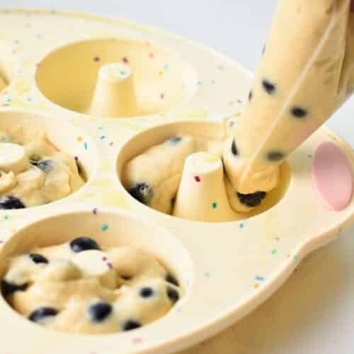 A piping bag filled with blueberry donuts batter filling a silicone donut pan.