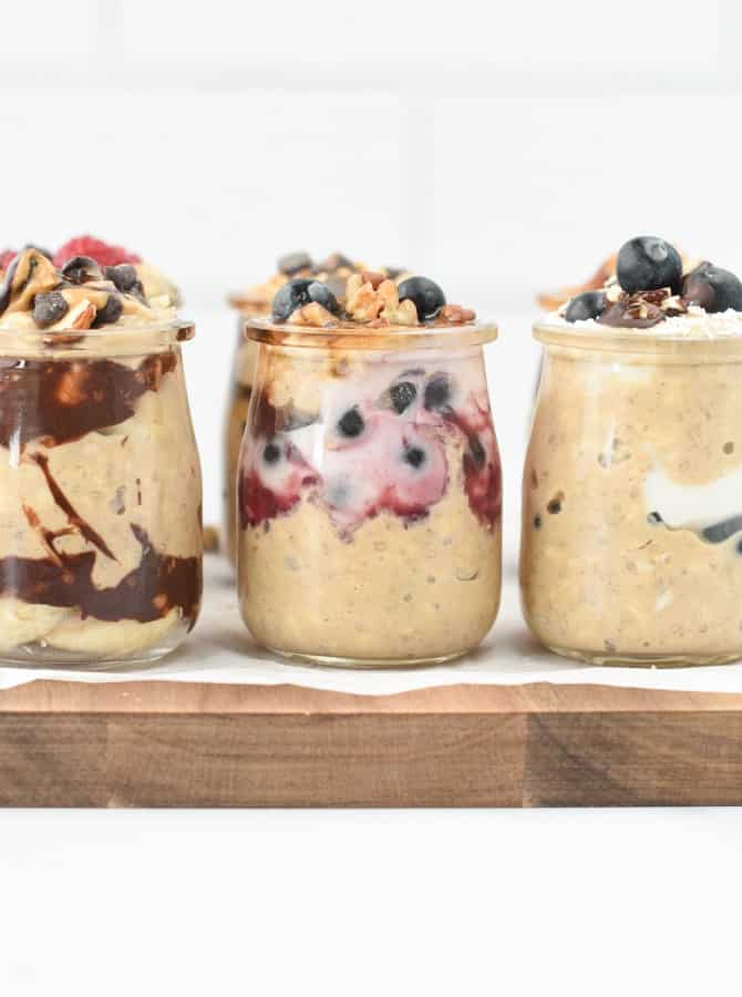 Six jar of protein overnight oats with various toppings on a wooden serving board.