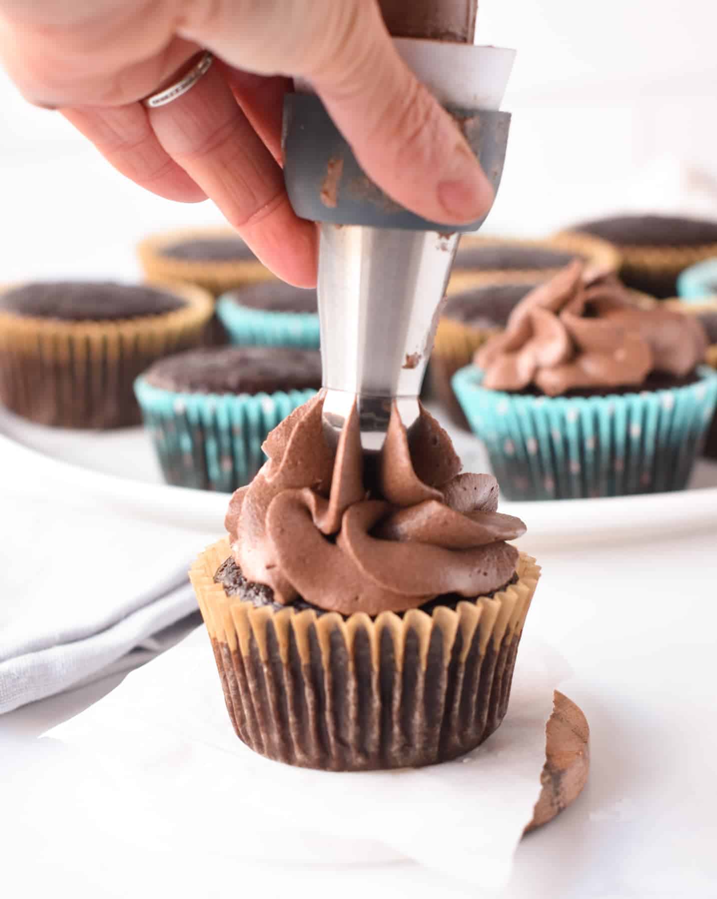 Piping vegan Cupcake Chocolate Frosting on a chocolate cupcake.