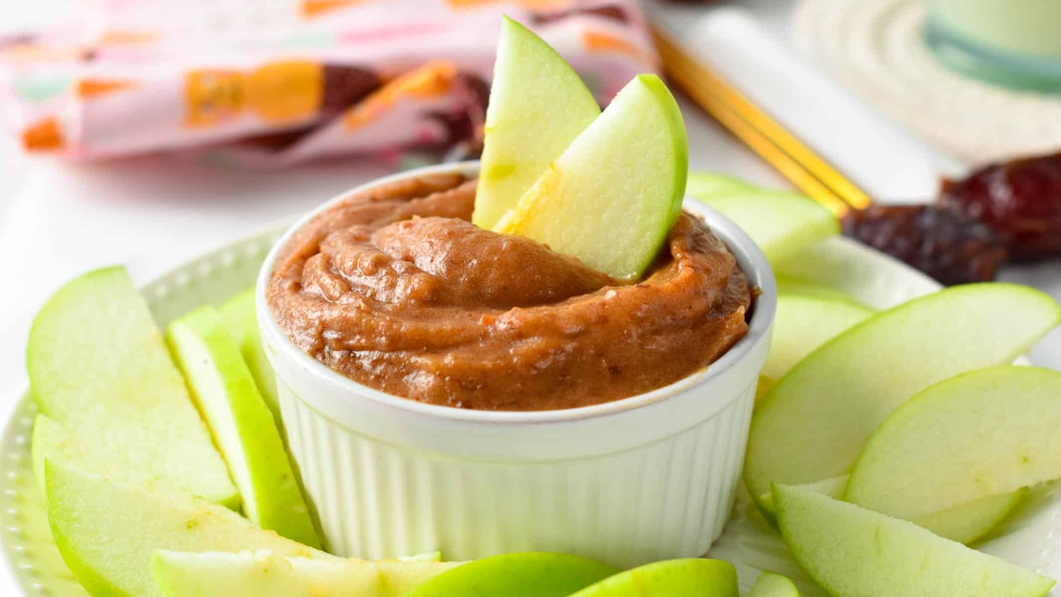 Date caramel sauce recipe in a small white ramekin with apple slices dipped into it.