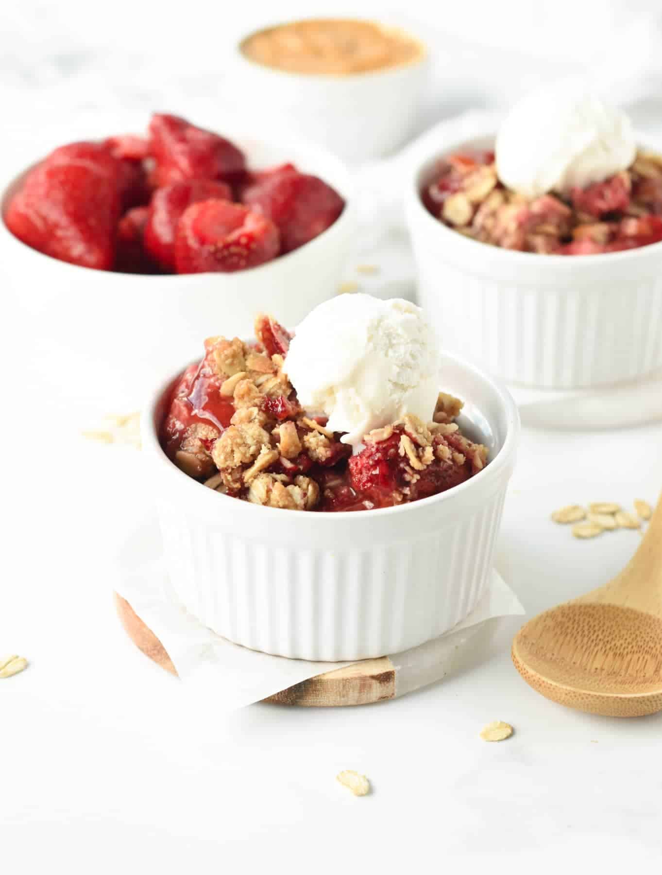 Strawberry Crisp in a small ramekin decorated with plant-based cream next to a wooden spoon.