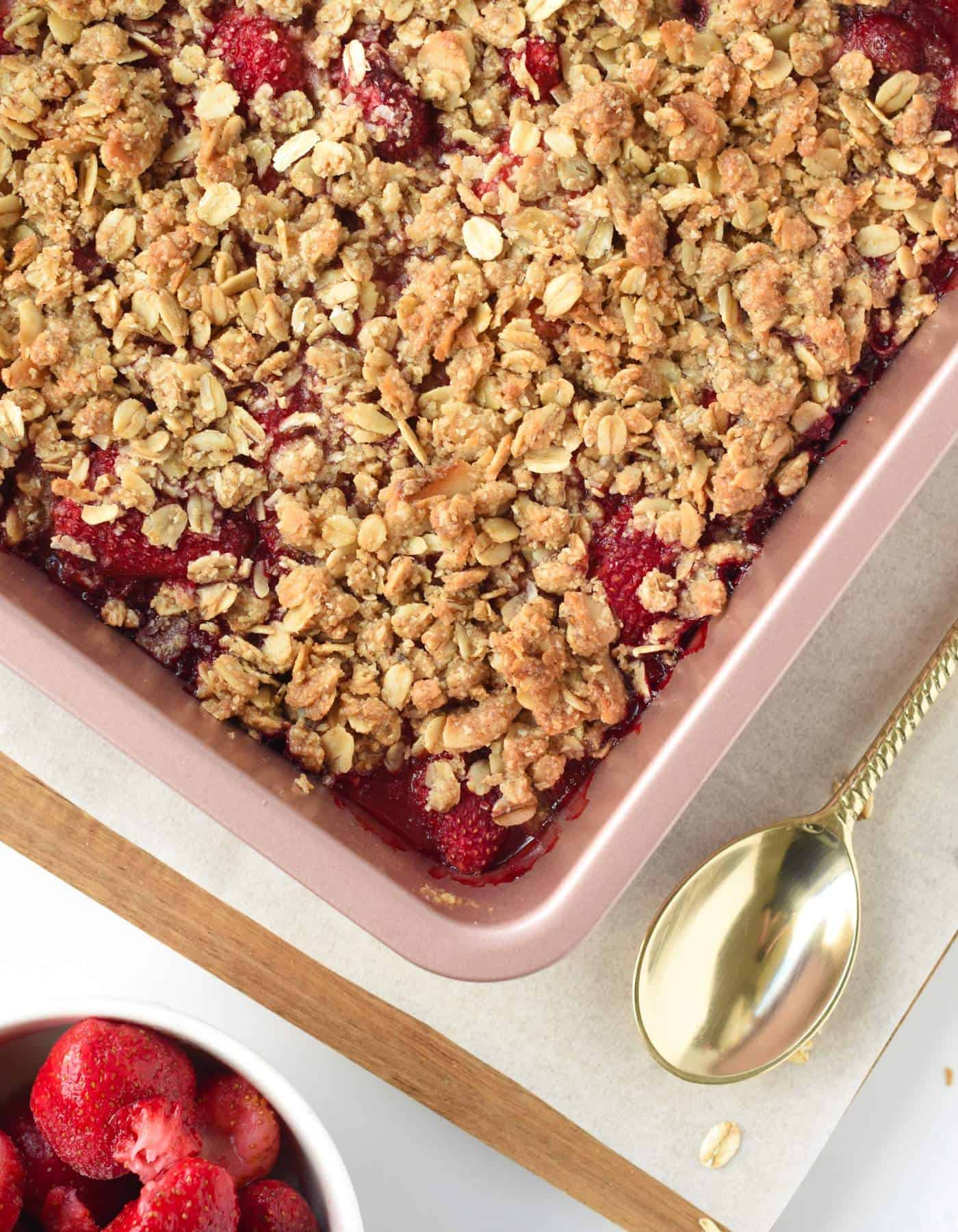 Strawberry Crisp in a large baking tray next to a golden spoon.
