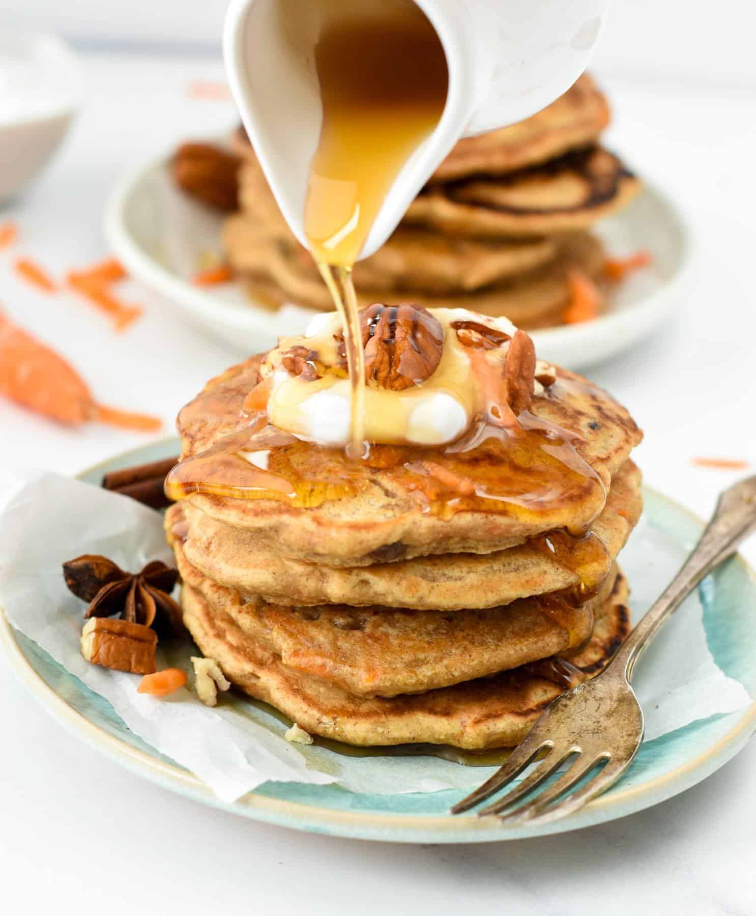 Carrot Cake Pancakes stacked on a plate with maple syrup poured on top.