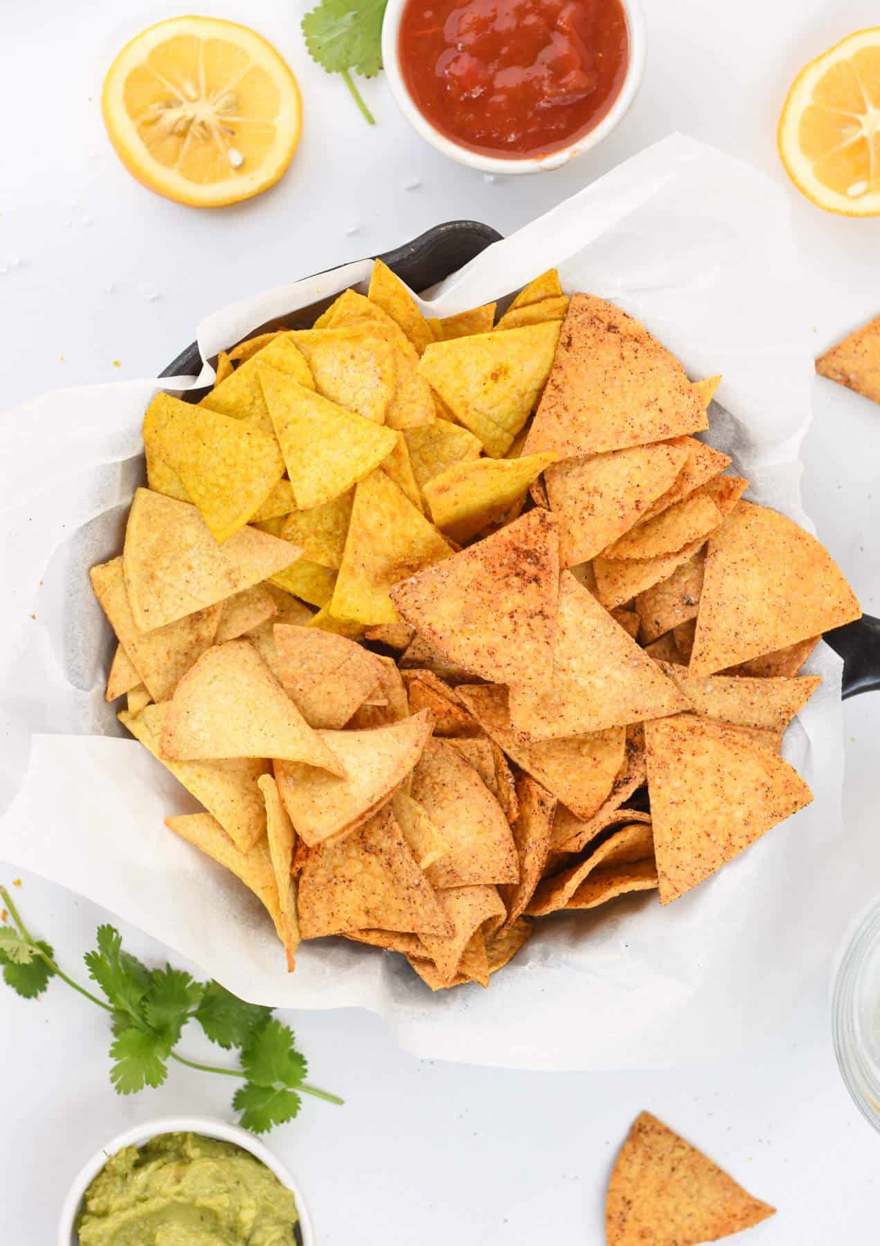 3 flavors of Air Fryer Tortilla Chips on a plate with guacamole and cilantro next to it.