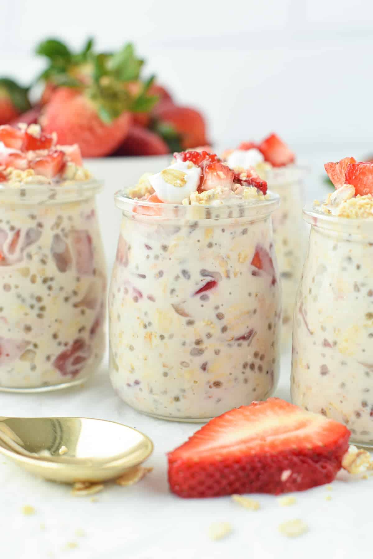 Overnight Oats in four jars, decorated with fresh strawberries.