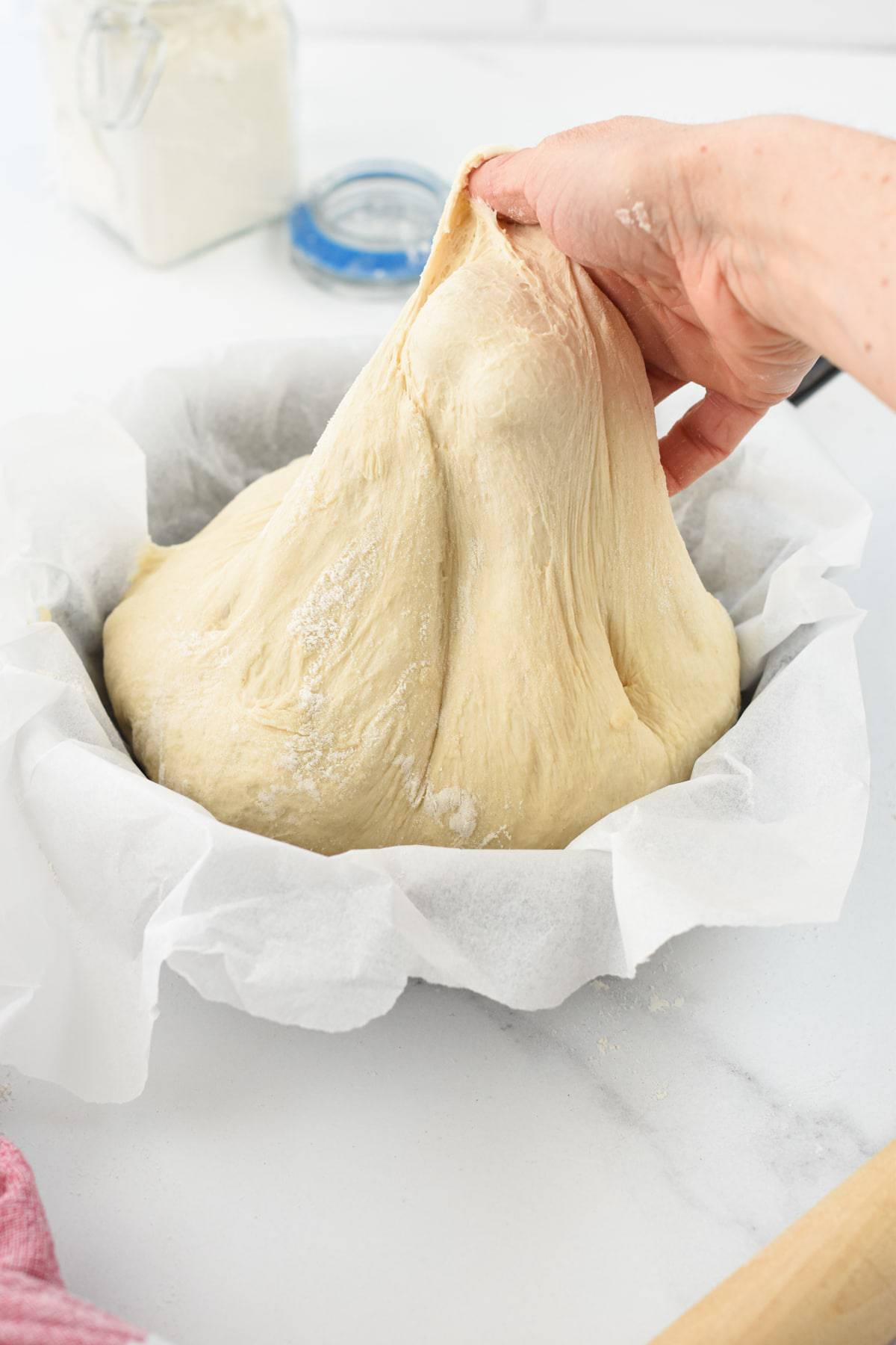 Pulling Spelt pizza dough out of a bowl with parchment paper.