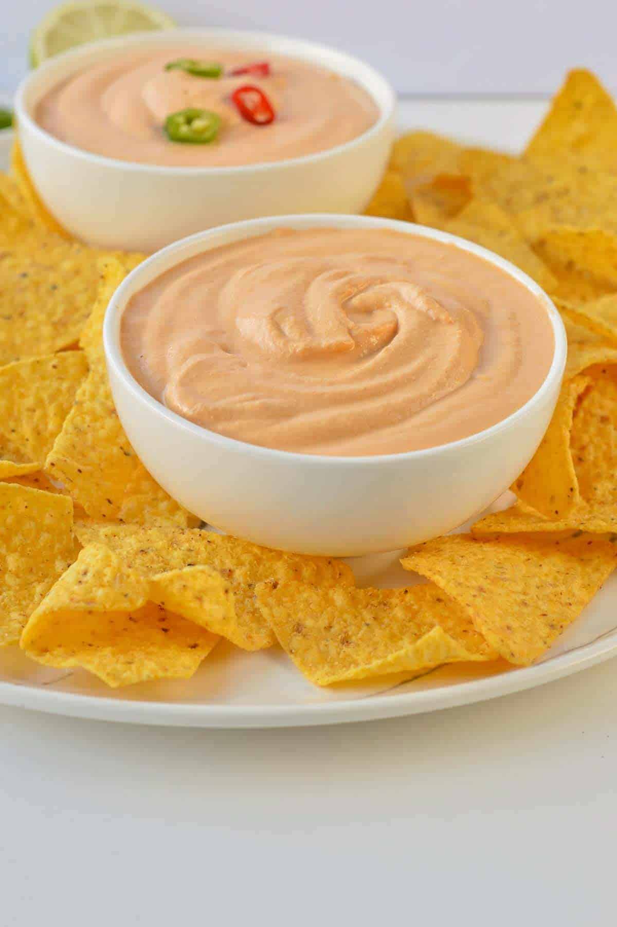 Bowl of vegan nacho cheese sauce on a plate filled with corn tortilla chips.