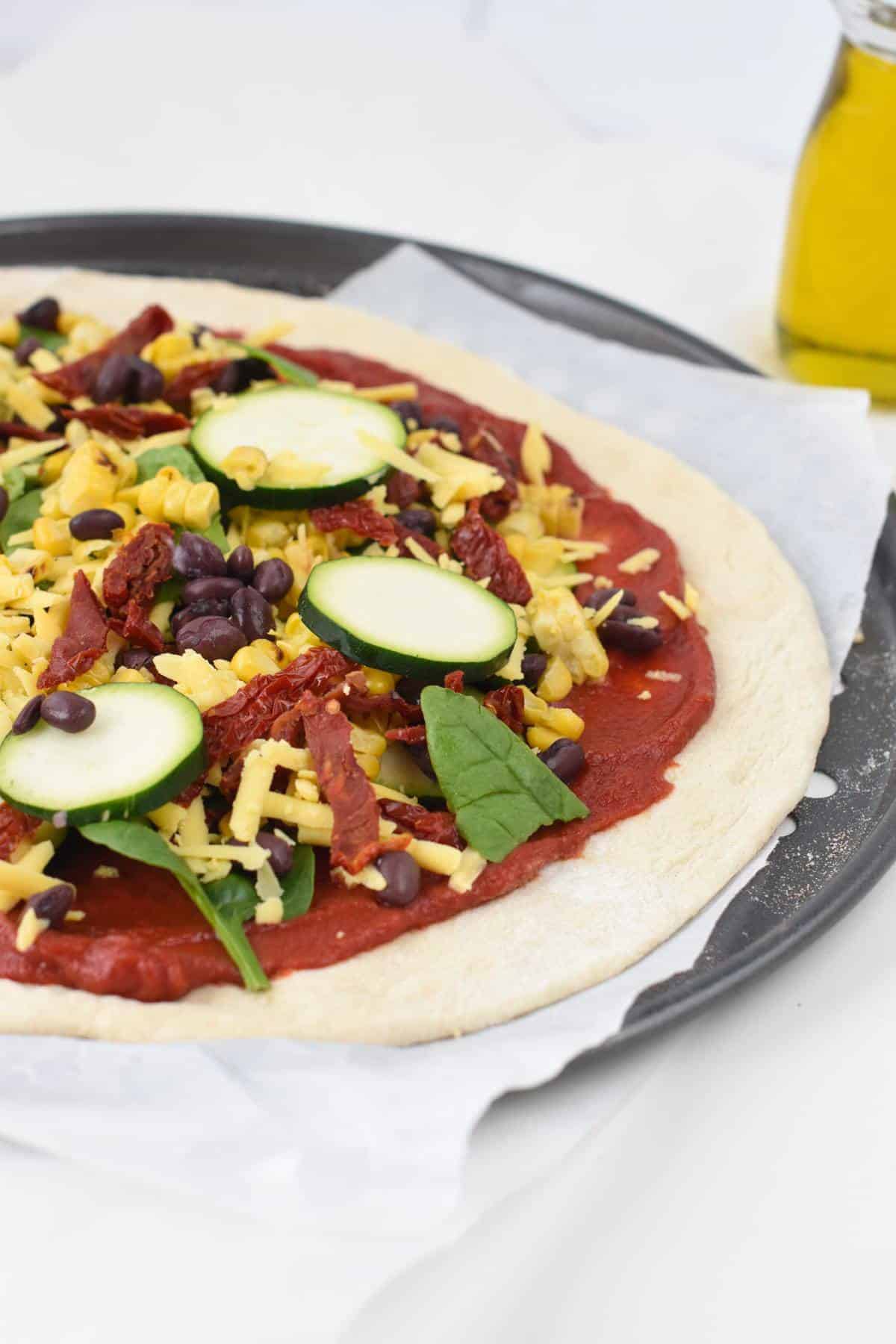 Vegan thin crust pizza dough with toppings on a pizza pan before cooking.