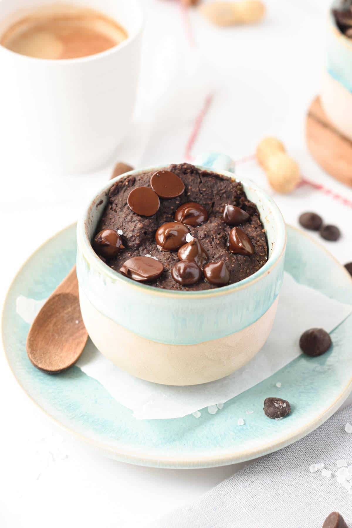 Vegan protein mug cake in a small mug with a coffee cup in the background